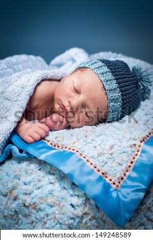 Newborn boy asleep on soft blue blankets, wearing a blue knit hat.