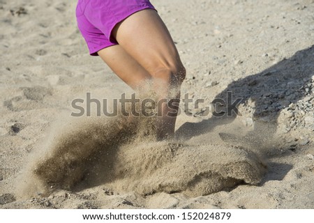 Young woman jumping in the soft sand making a splash at the end of her trail run at South Mountain Park in Phoenix, Arizona.