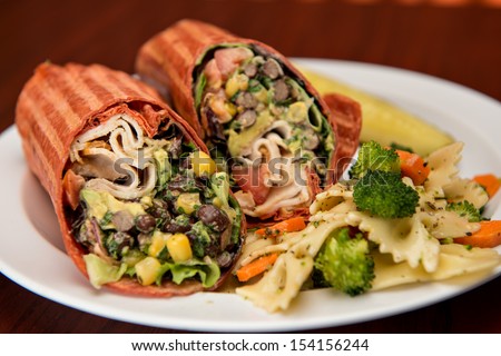 Southwest chicken wrap sliced in half on a white paper plate with a side of pasta salad.