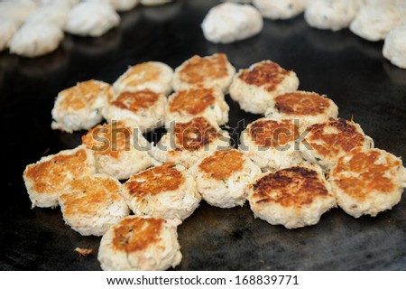 Mini crab cakes cooking on a hot griddle.