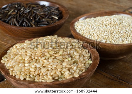 Small wood bowls filled with brown rice, quinoa and wild rice. This is shot on a wood table.