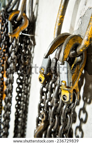 Several large industrial weathered yellow hooks attached to chain and a pulley.