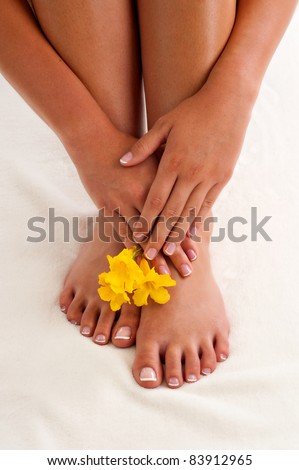 Woman\'s french manicured hands positioned above her french pedicured feet.  There is also 3 yellow flowers pictured.