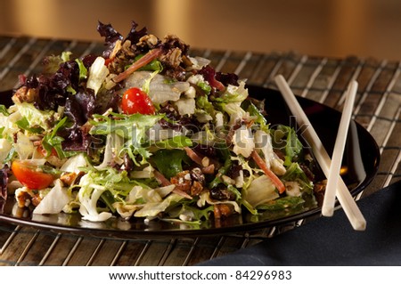 Close up of a fresh chopped salad on a black plate.  Chop sticks are also featured.