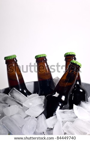 Four brown beer bottles on ice with bright green caps shot on white.
