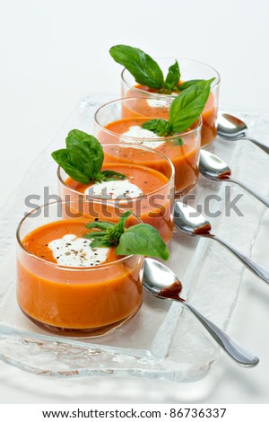Four small glass bowls filled with tomato soup along side sliver spoons.