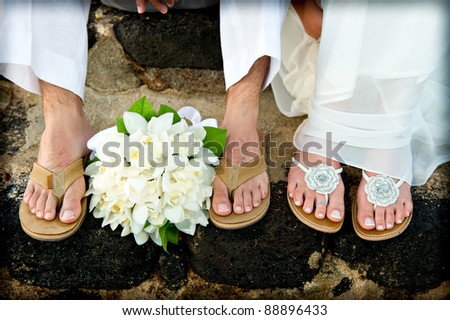 Close up of a bride and groom\'s feet and bouquet. They had just gotten married on the beach and are wearing sandals.