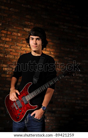 Portrait of a teenager with one hand in his pocket and the other on his red guitar.  Studio shot.