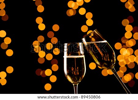 Pair of champagne flutes toasting on a black background with out of focus yellow and orange lights. Studio Shot.