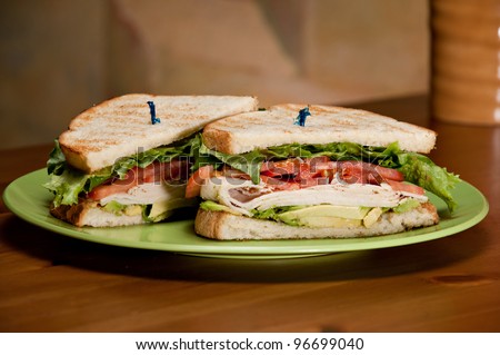A deli classic turkey sandwich with plenty of turkey, avocado, tomato, and lettuce on white toasted bread.