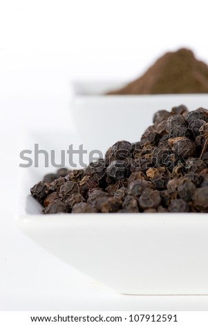 Black pepper grain and powder in ceramic bowl