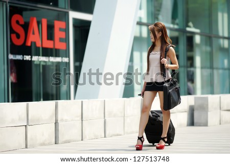 Young business woman walking outside of shopping plaza with her rolling luggage and briefcase. (shallow DOF)