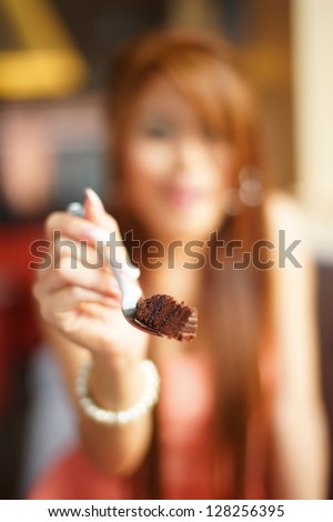Young beautiful woman sitting in cafe eating  chocolate cake. Focus on cake.