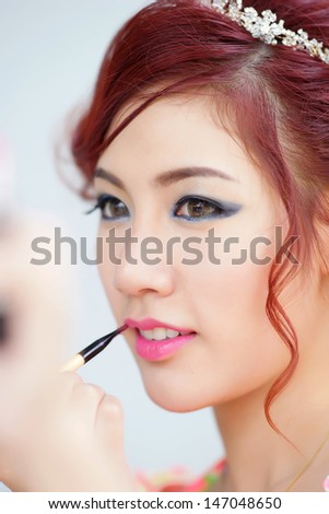 Beauty woman applying lipstick on lips with brush, Model is Thai Ethnicity.