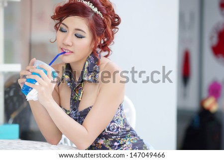 Young beautiful woman sitting at outdoor cafe holding soft drink glass, Model is Thai Ethnicity.