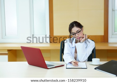 Attractive young female doctor sitting at desk in office doing paperwork.