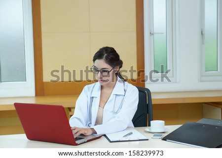 Attractive young female doctor sitting at desk in office typing on computer