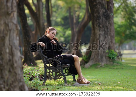 Beautiful Asian lady in black dress, posing in the park, greenery in the background, model is Thai Ethnicity.