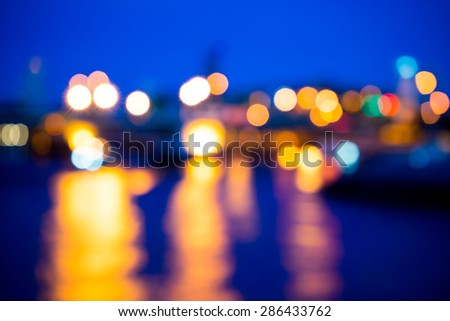 View of night light blur with reflection light in water on twilight background at bridge in Bangkok, Thailand
