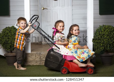 one red head boy pushing lawn mower with two beautiful twin girls sitting on it