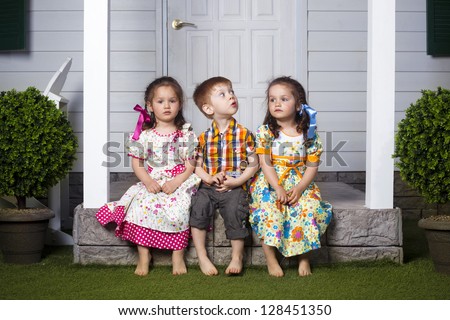 two beautiful twin girls and one red head boy are sitting together on the porch of white mansion house