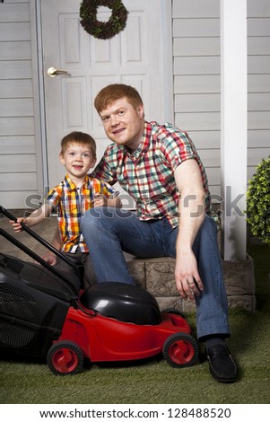 red head father and son sitting on the porch of country house with lawn mower