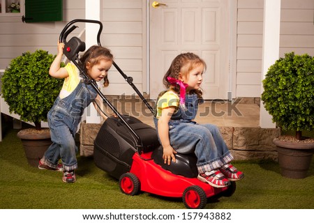 two beautiful twin girls riding and pushing lawn mower in front of the summer house