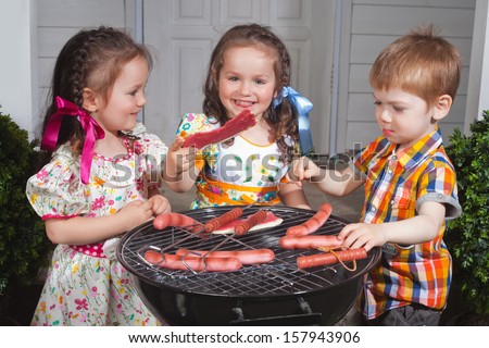 two beautiful twin girls and one red head boy eating barbecue and playing in summer garden