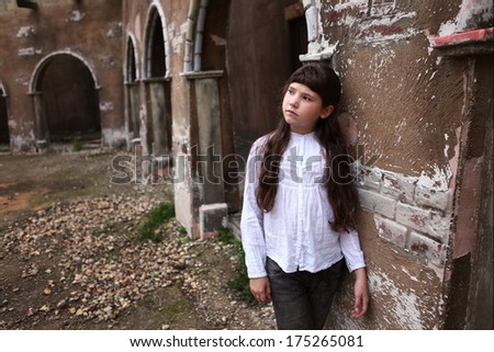 little pretty preteen girl with long dark hairs in the yard of old abandoned house of 17 th century