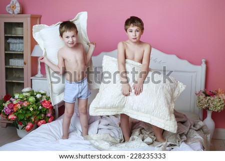 two boys prepare for pillow fight in cozy pink bedroom interior background