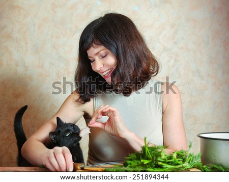 pretty housewife cut chicken on the kitchen table and black cat ask for meat