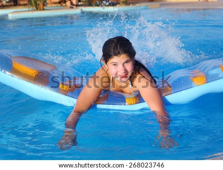 preteen girl in swimming suit with inflatable matrass in the open air swimming pool in the beach hotel resort