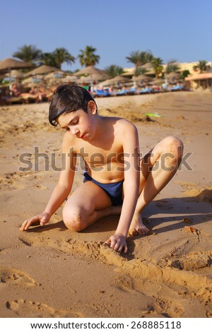 preteen handsome boy play with sand on the red sea beach and yaht background