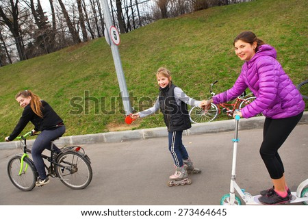 happy girl friend ride roller skates scooter and bicycle on tow laughing happily