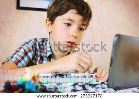 preteen handsome boy make rainbow loom toy with on line lesson on tablet computer