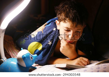 preteen handsome boy read book with lamp before sleep