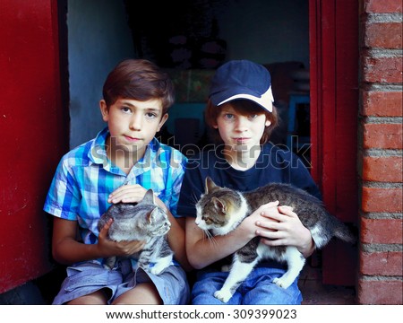 two preteen boys with cats on knees sit on the house porch
