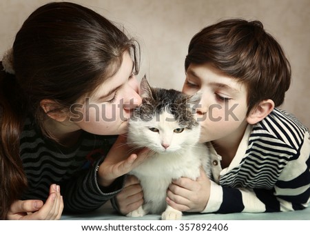 two teenager siblings boy and girl kiss siberian fat cat on cheeks close up indoors portrait
