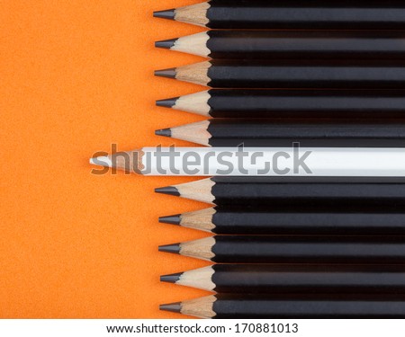 White pencil placed between black pencil on orange background