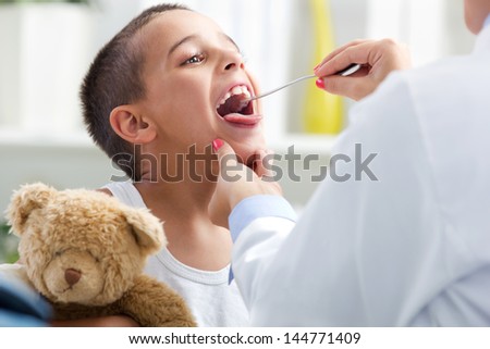 young doctor examining child\'s throat,child holding a teddy bear in hands