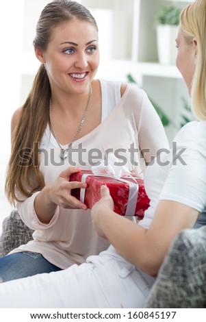 Merry caucasian woman giving a present to her surprised friend for her birthday at home