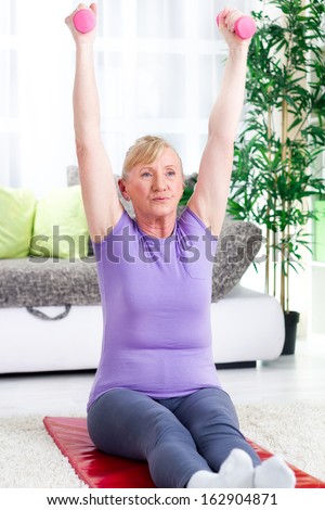senior woman sitting on a mat at home and exercise with weights