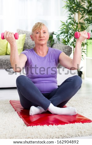 senior woman sitting on a mat at home and exercise with weights