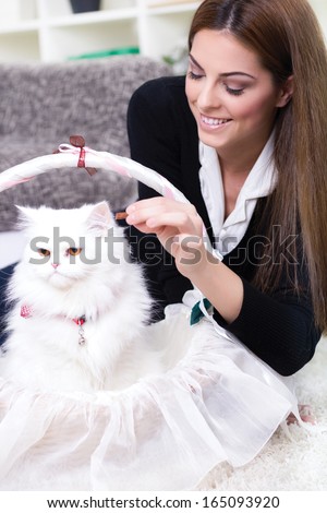 young woman feeding a white Persian cat at home