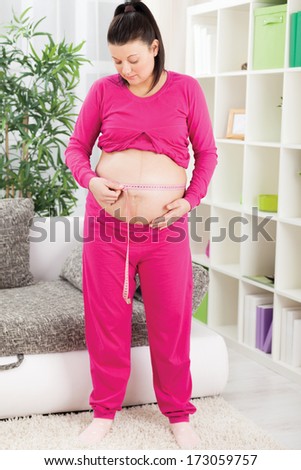 happy pregnant woman measures her belly at room