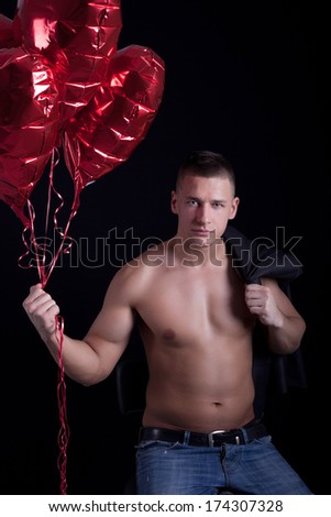 muscular young man holding a heart shaped balloon against black background