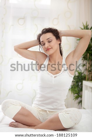 sleepy woman waking up and yawning with a stretch while sitting in bed