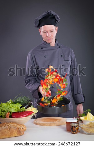 male chef tossing vegetables from wok in kitchen