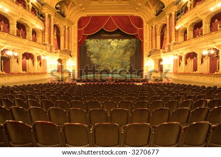 Theater stage with red velvet curtains and empty chairs in the foreground
