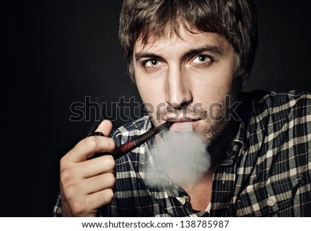 Artistic dark portrait of the young beautiful man smoking a pipe